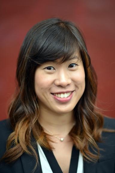 Woman with long dark brown hair smiling in front of a red background.