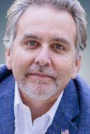 Man with short silver hair and beard smiling and wearing a blue blazer over a white collared shirt