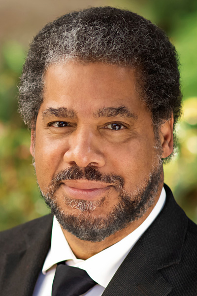 Man with short black and white hair and beard, wearing a suit and tie