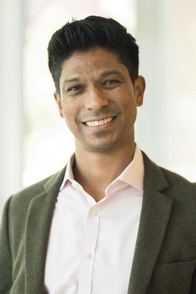 Man smiling with short dark hair wearing a white shirt and blazer